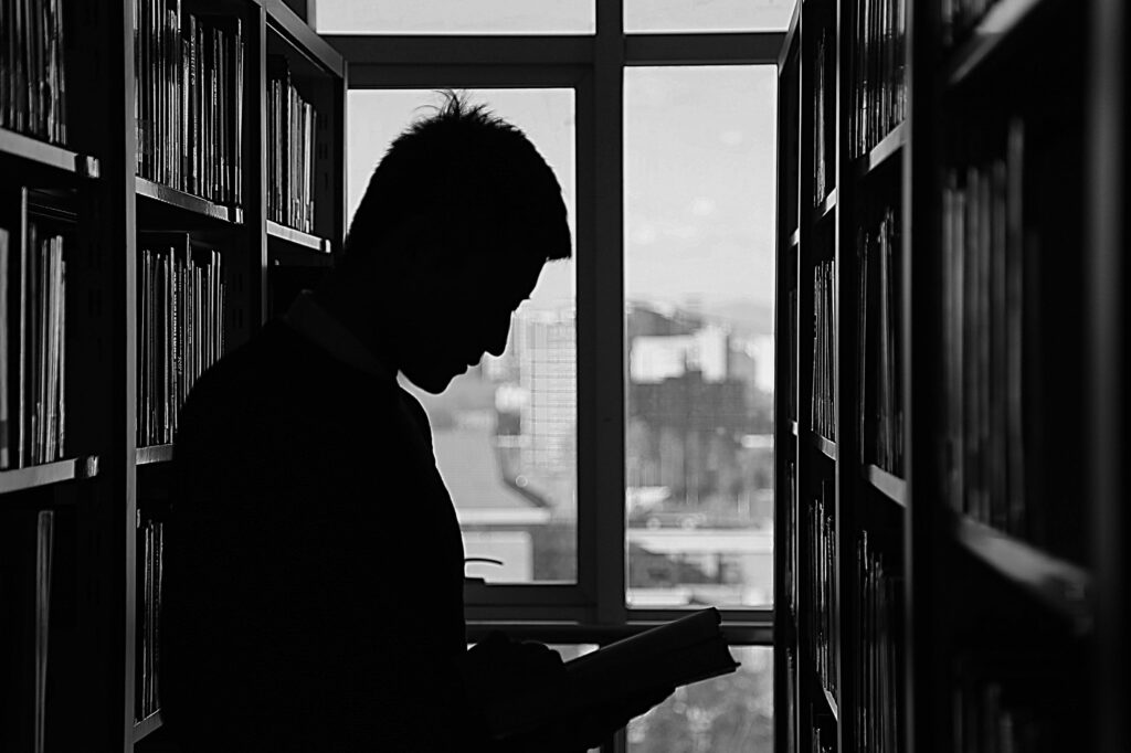 A moody silhouette of a man reading in a library, capturing solitude and contemplation.